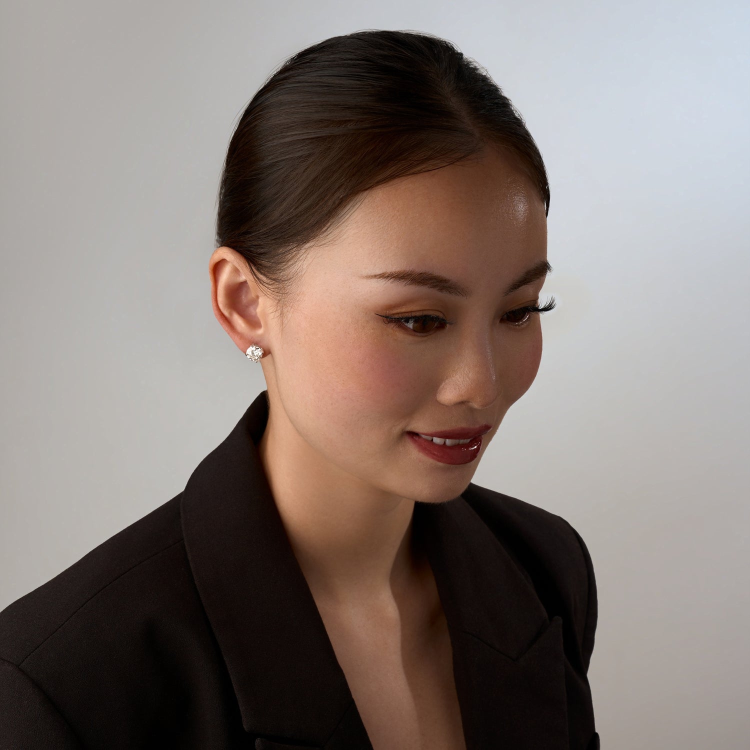 Woman with a sparkling moissanite earring, wearing a black blazer against a plain background