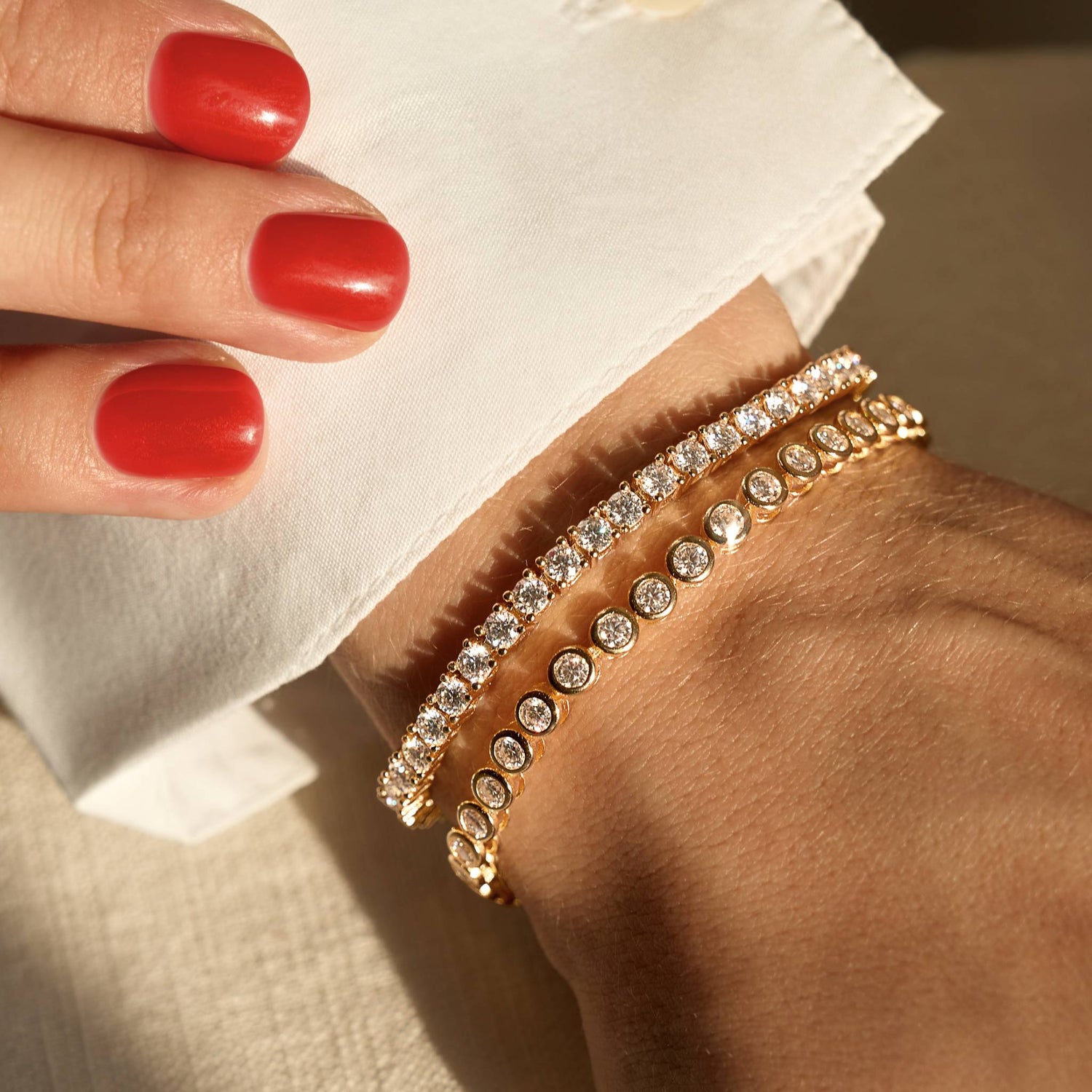Gold moissanite bracelets with clear stones on a wrist with red nail polish.