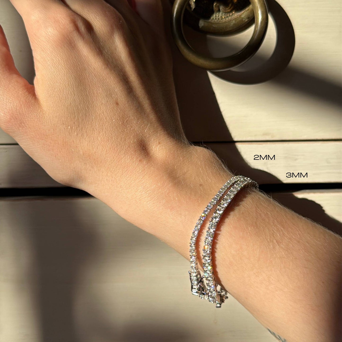 Close-up of a wrist wearing two diamond bracelets with size labels in the background.