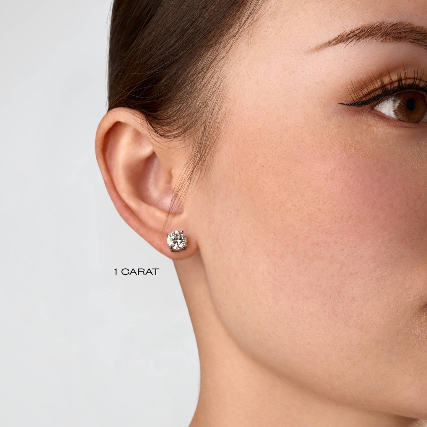 Close-up of a moissanite round cut stud earring on an ear with a neutral background