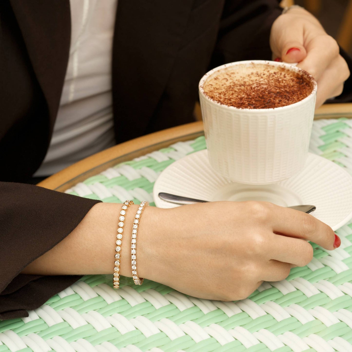 Person holding a white mug with a hot beverage on a green checkered tablecloth showcasing her 18k gold plated tennis bracelets.