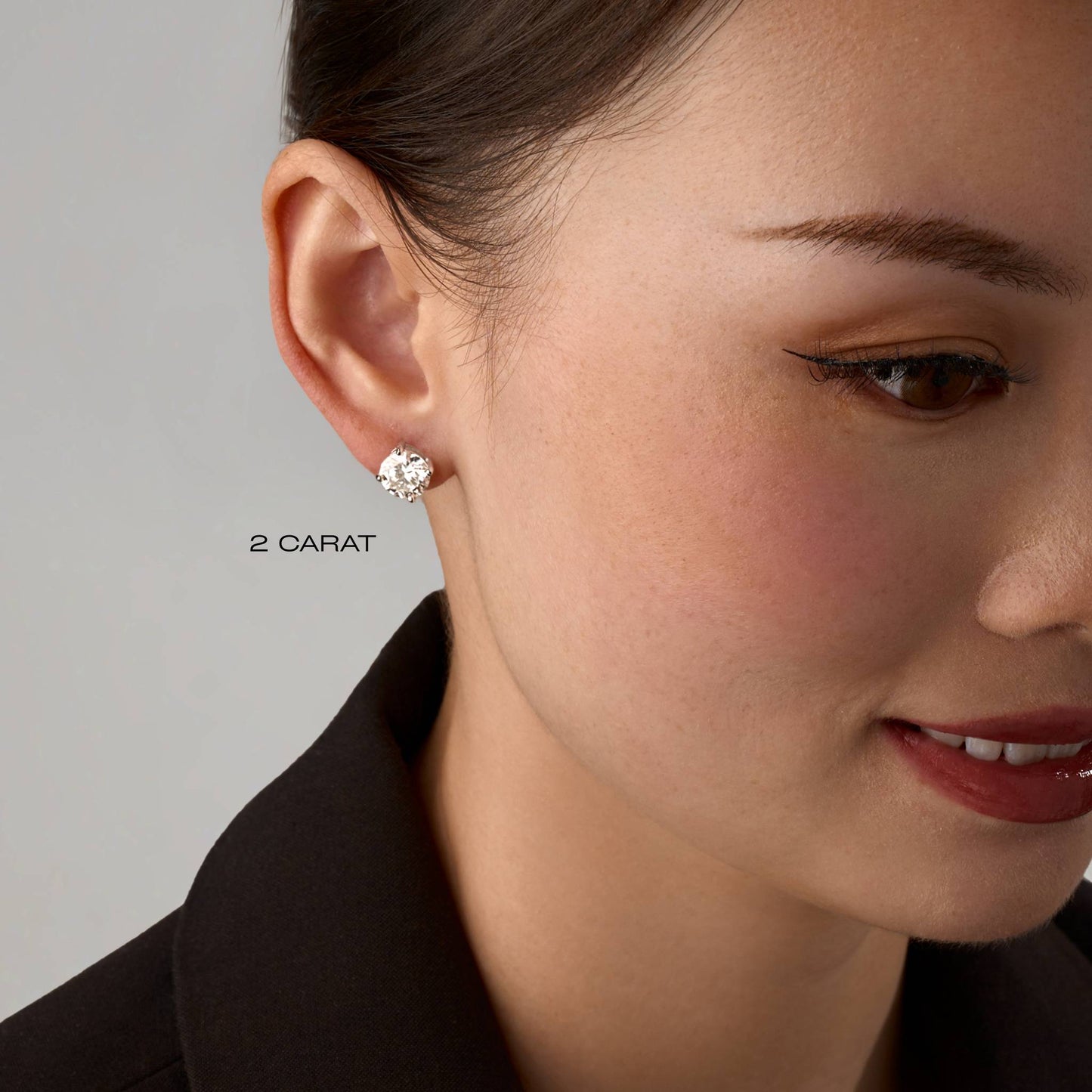 Close-up of a woman wearing a diamond earring with '2 Carat' text on a neutral background