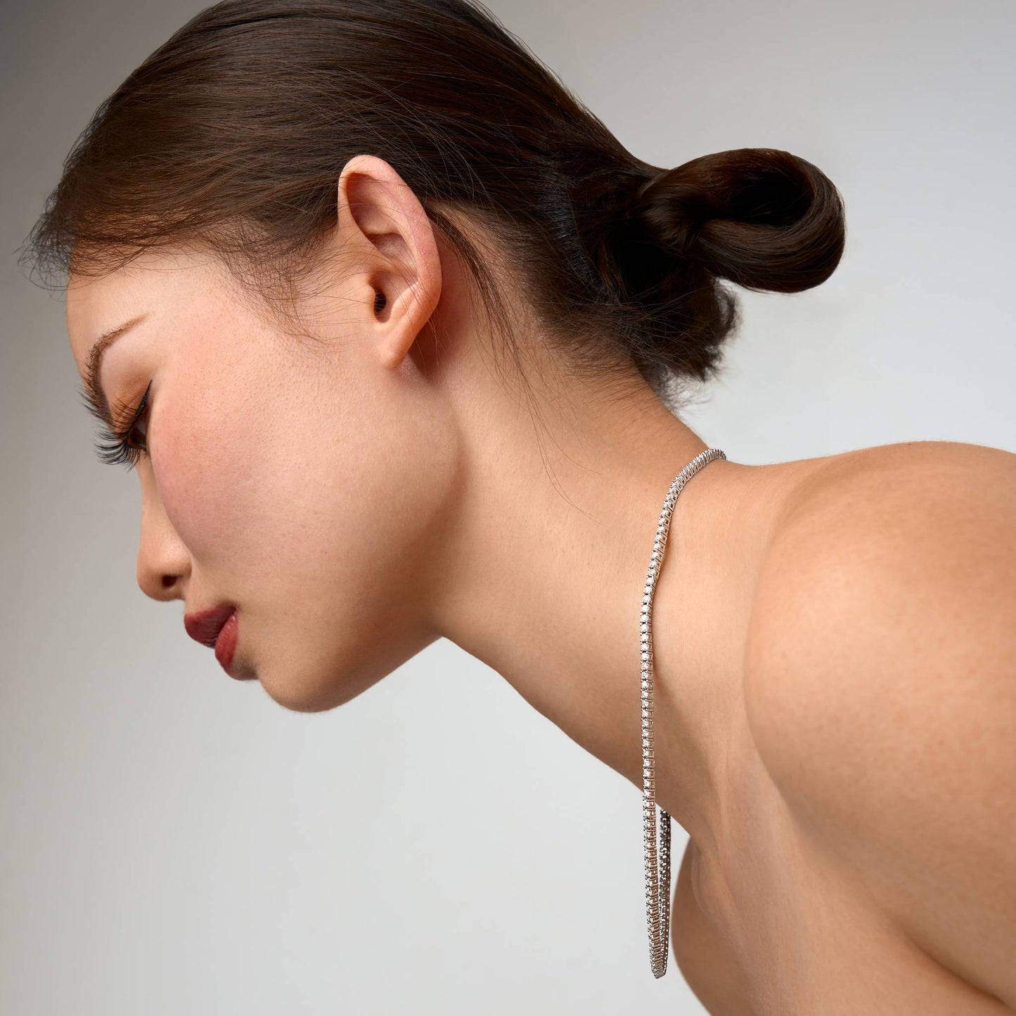Woman wearing a silver tennis necklace against a neutral background