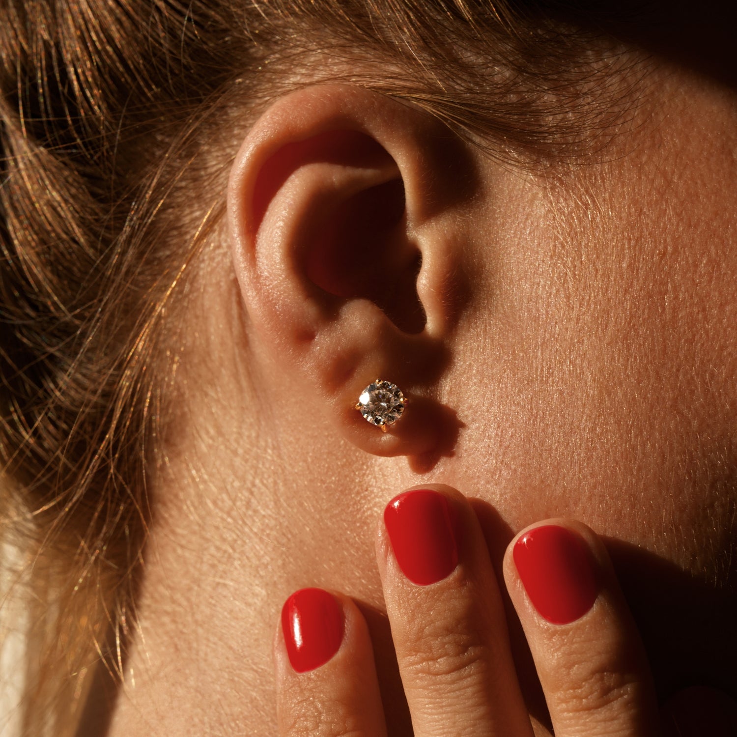 Close-up of an ear with a moissanite earring, hand with red nails touching the cheek