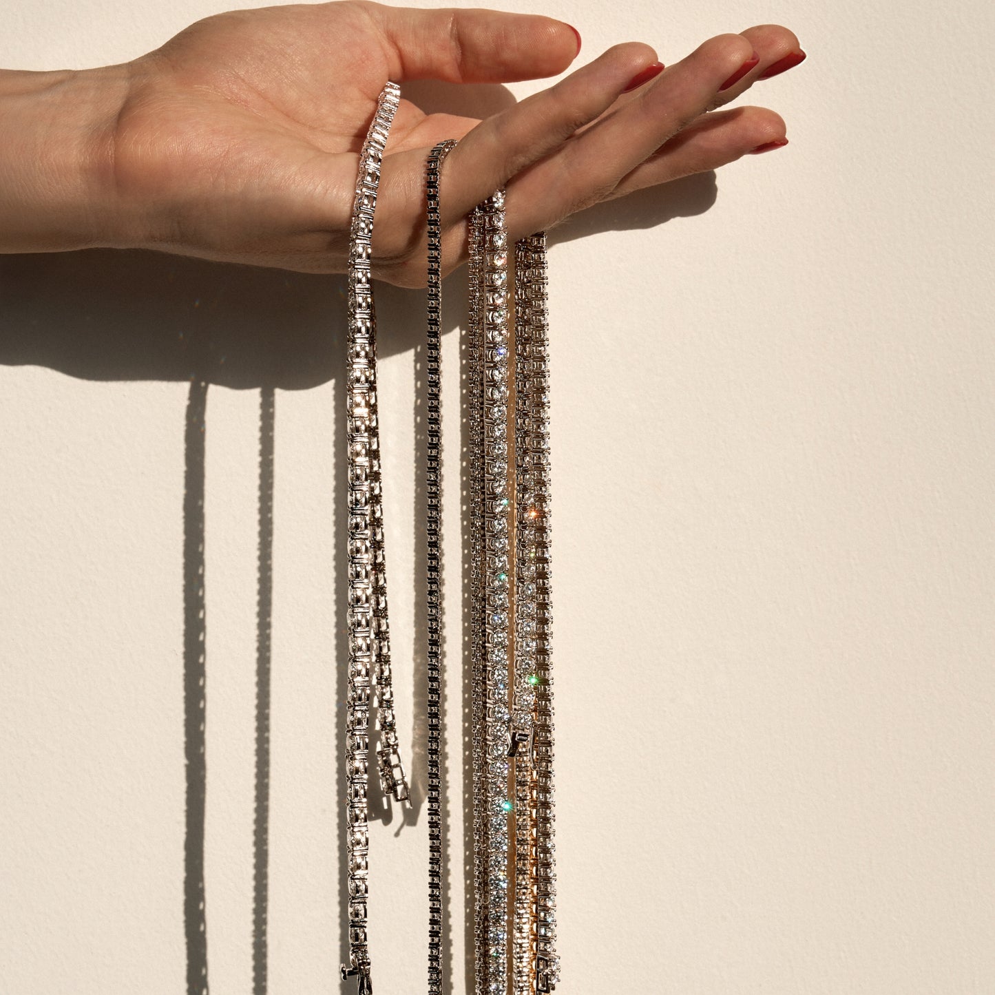 Hand holding multiple moissanite necklaces against a neutral background