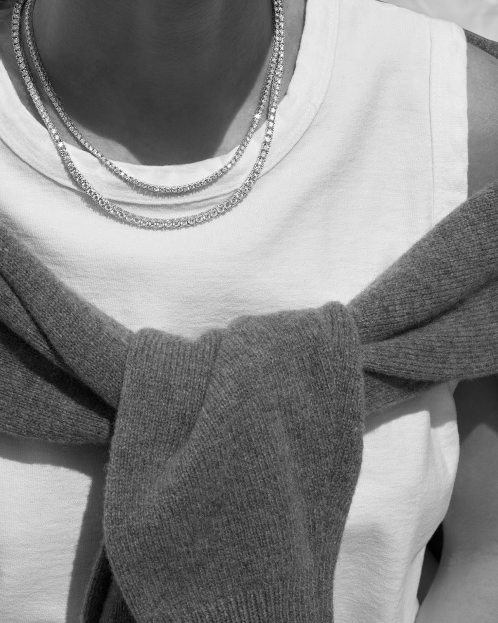 Close-up of a person wearing a gray sweater and multiple moissanite necklaces.
