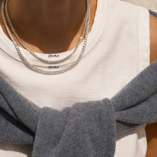 Close-up of a person wearing two silver chain necklaces with measurements on a neutral background.