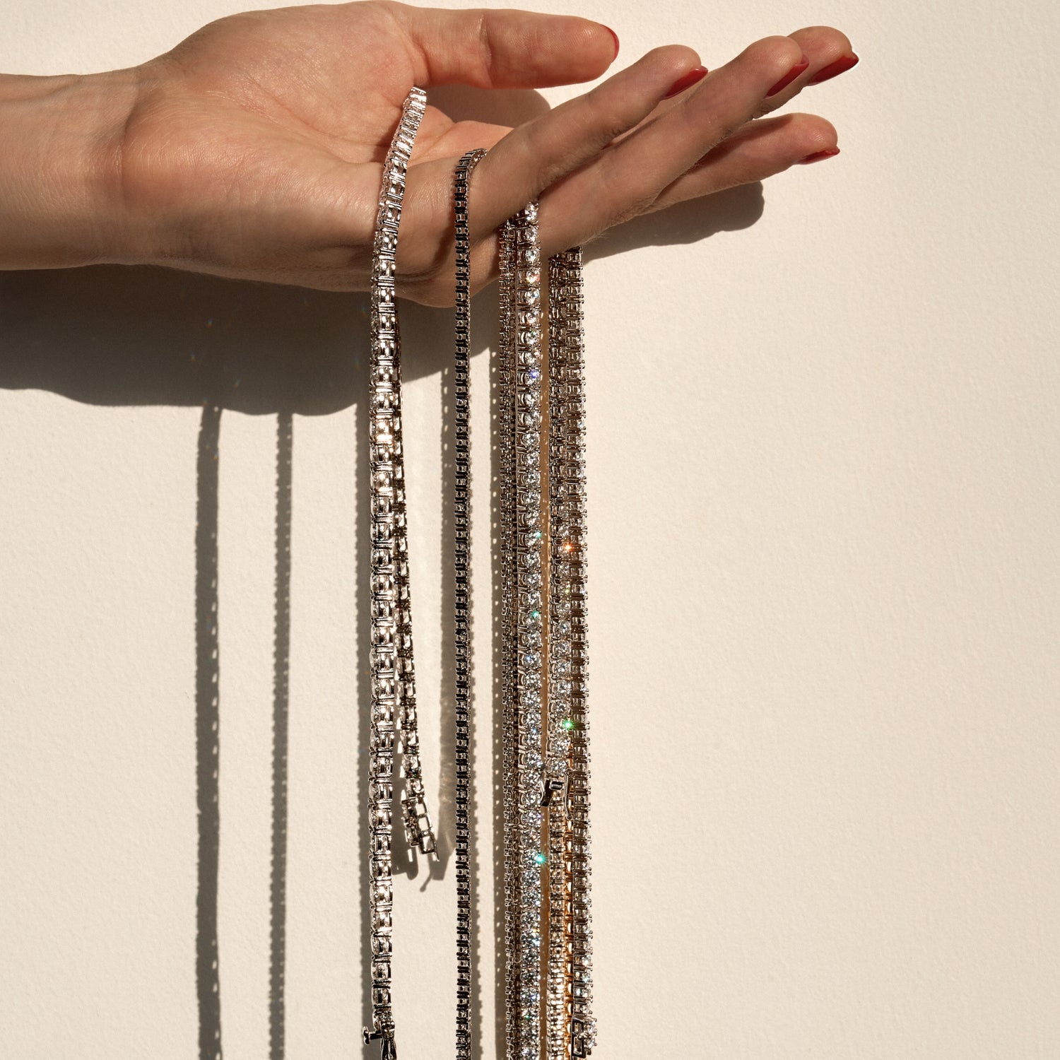 Hand holding multiple luxury necklaces against a neutral background