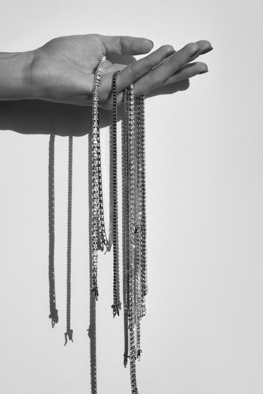 Hand holding multiple moissanite tennis necklaces against a plain background in black and white